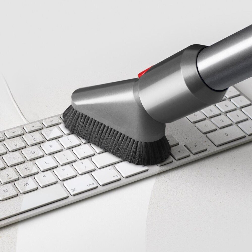 Odkurzacz z nasadką szczotkową czyści białą klawiaturę.