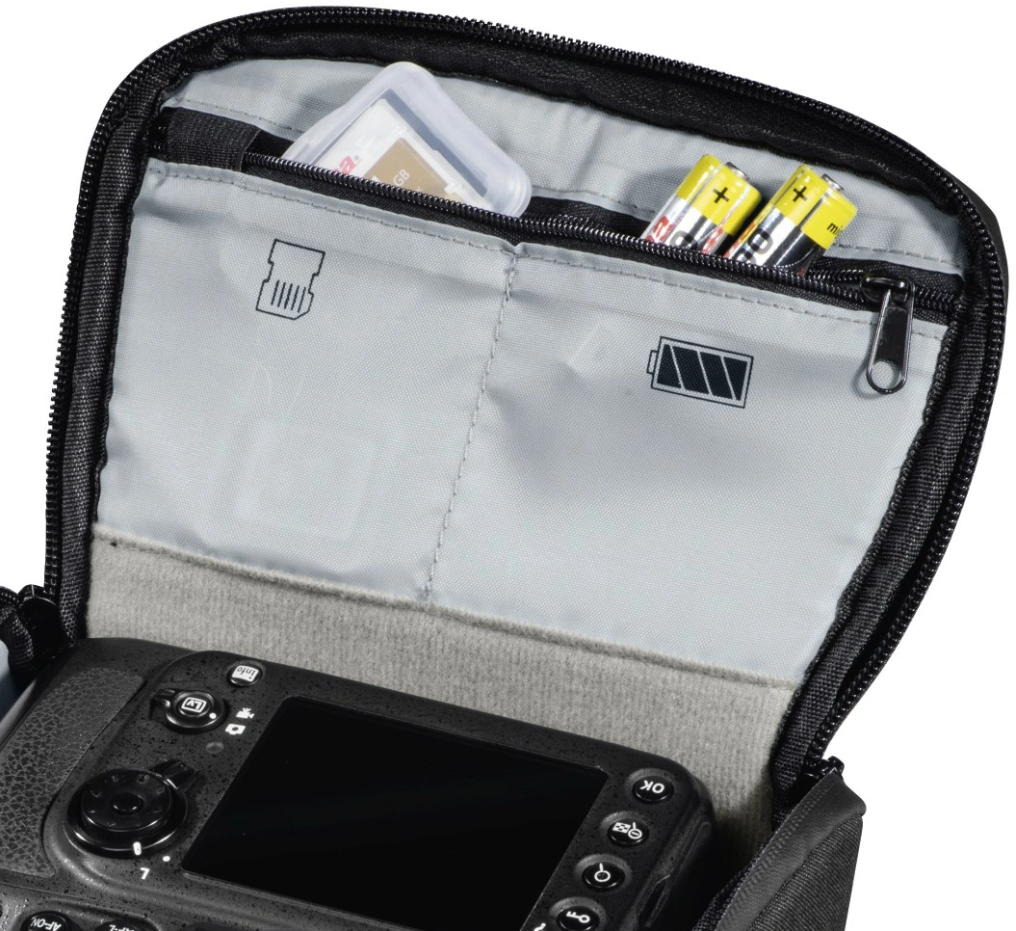 Open camera bag shows SD card, two AA batteries, and a camera's top with buttons.
