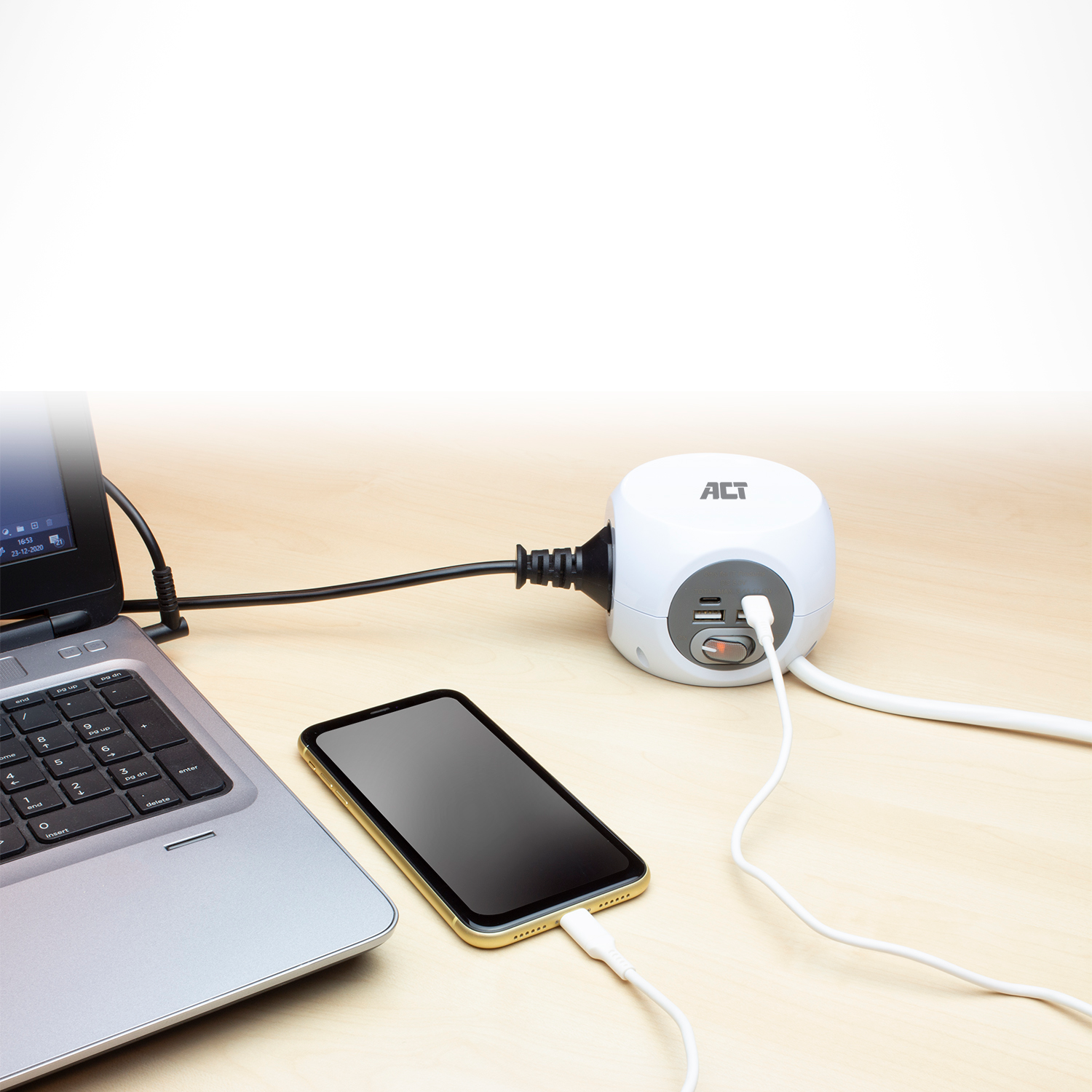 Een witte power cube met stopcontacten en een telefoon en laptop aangesloten op een houten oppervlak.