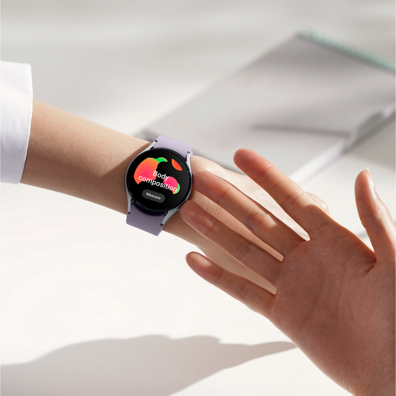 Een pols met een paarse smartwatch. De watch toont 'Lichaamssamenstelling'. Een hand is in beeld.