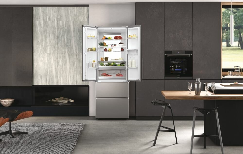 Lodówka ze stali nierdzewnej z otwartymi drzwiami, wypełniona jedzeniem. Kuchnia z drewnianą podłogą i ciemnymi szafkami.