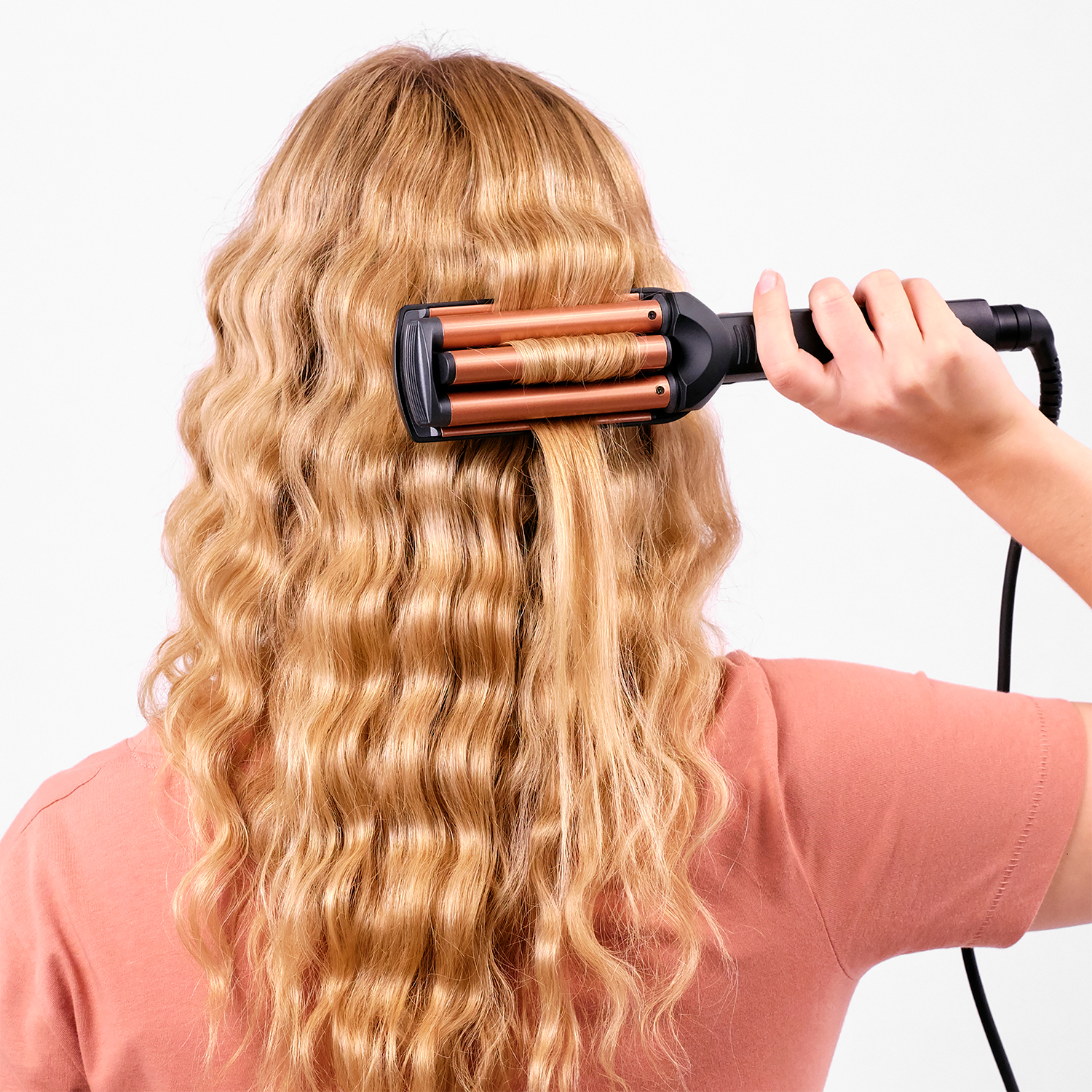 Una donna usa un'arricciacapelli su capelli biondi e ondulati.