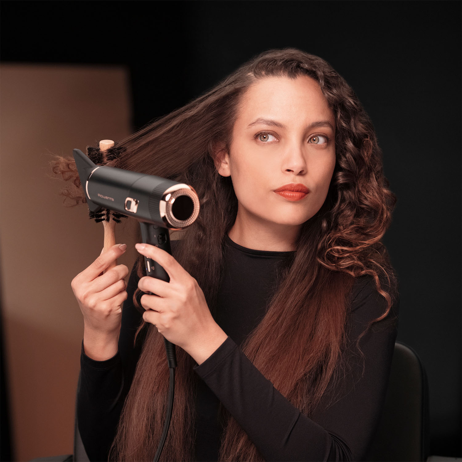 Donna che usa un asciugacapelli con una spazzola rotonda. Guarda in alto, si sta acconciando i capelli.