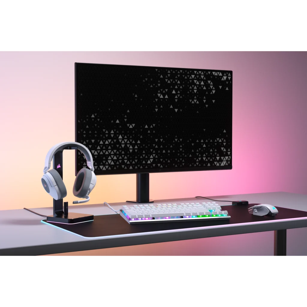Gaming setup: monitor, fejhallgató, billentyűzet és egér fekete-rózsaszín asztalon.