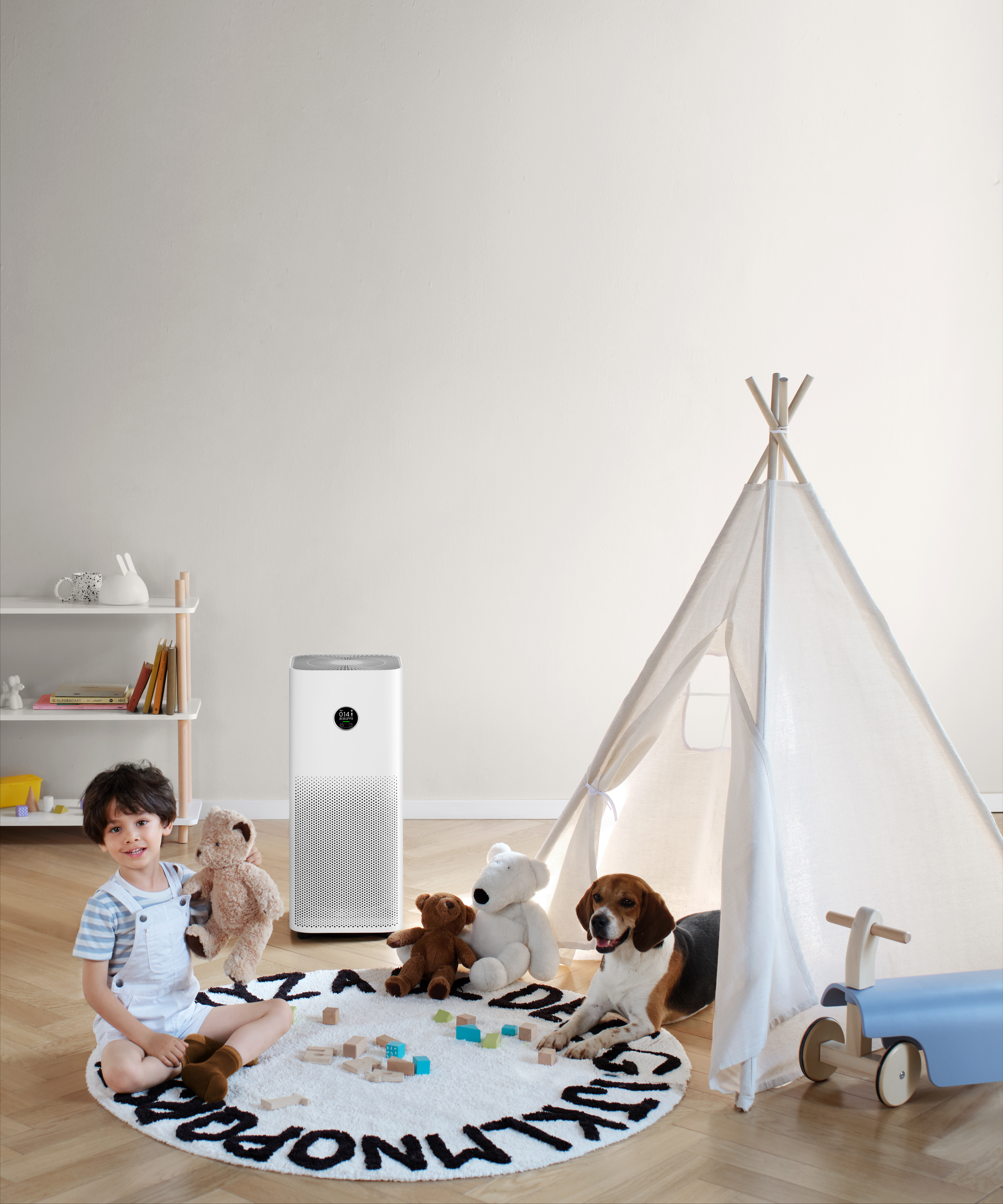 Bir çocuk, oyuncaklarla birlikte bir hava temizleyici ve bir çadırın yakınında oturuyor. Bir köpek çadırın yanında dinleniyor.