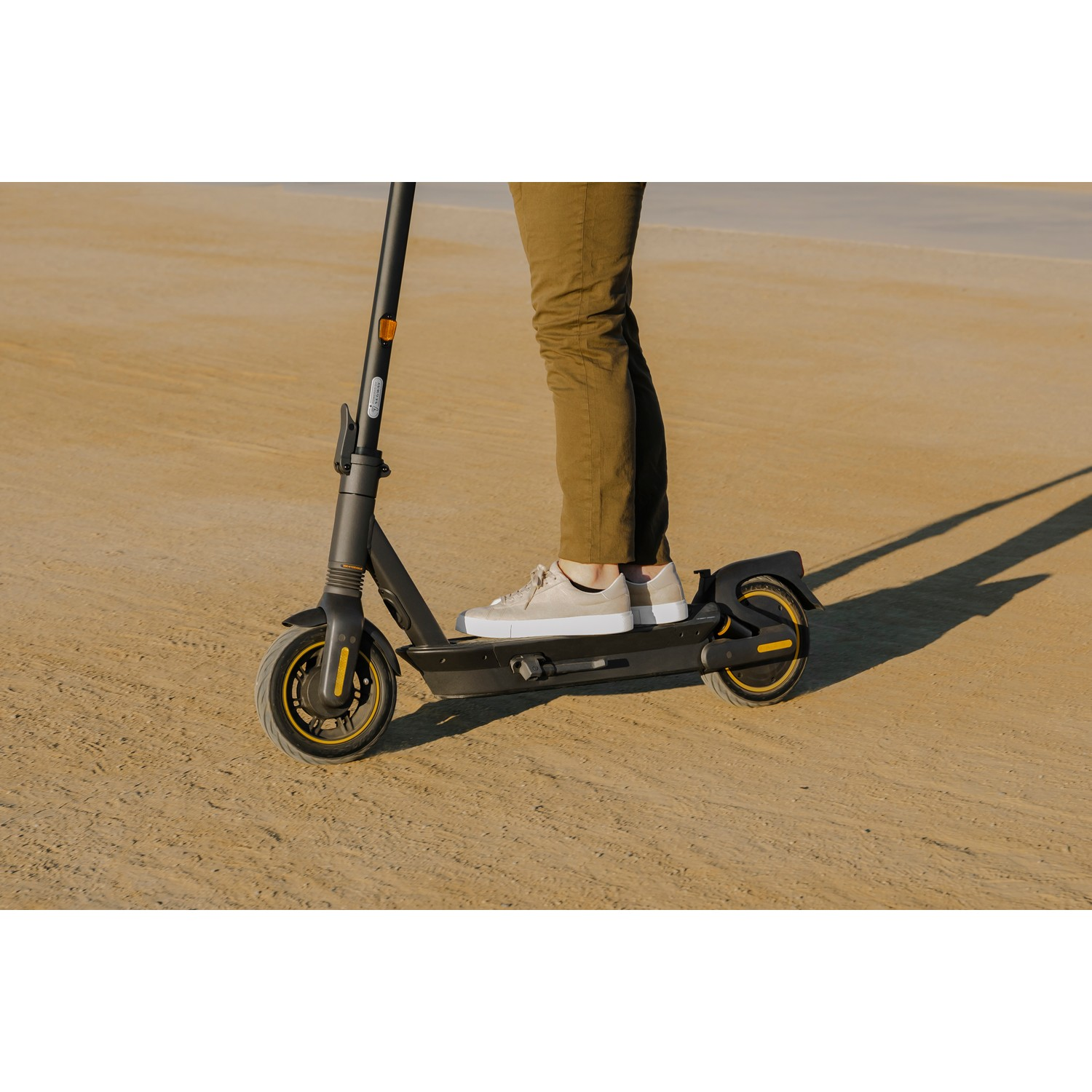 Personne conduisant une trottinette électrique noire et jaune sur une surface sablonneuse.