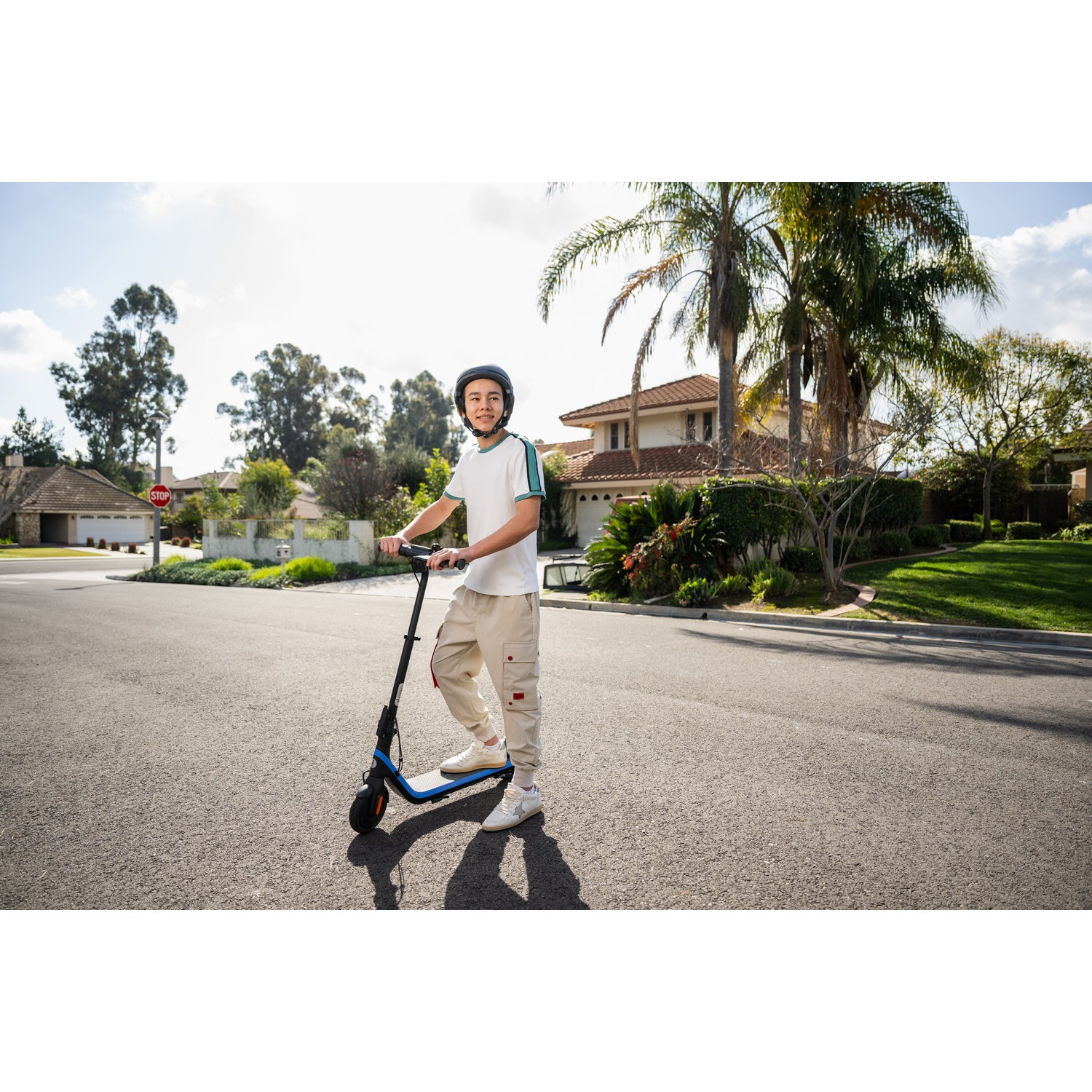 A young man on an electric scooter on a residential street, sunny day.
