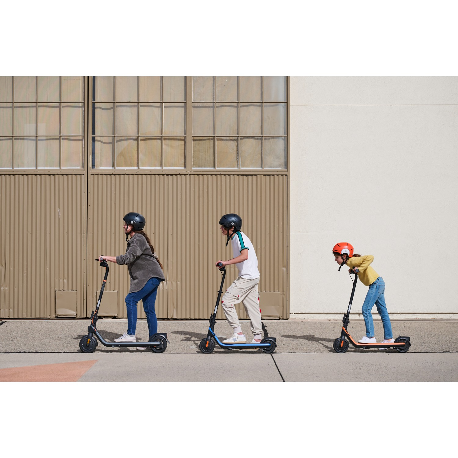 Drie personen rijden op scooters op een stoep. Ze dragen allemaal helmen.