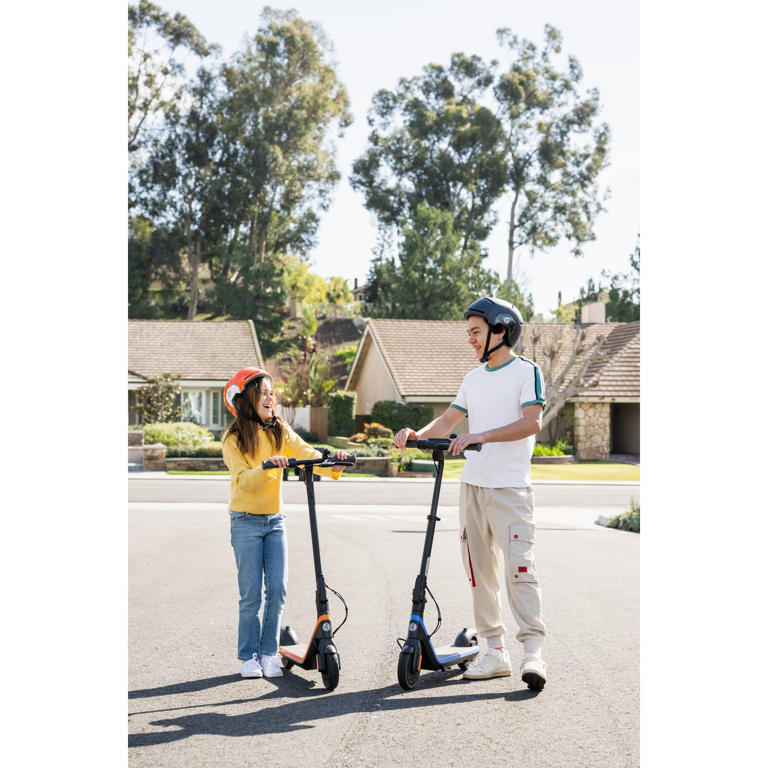 Twee kinderen op elektrische scooters op een voorstedelijke straat.