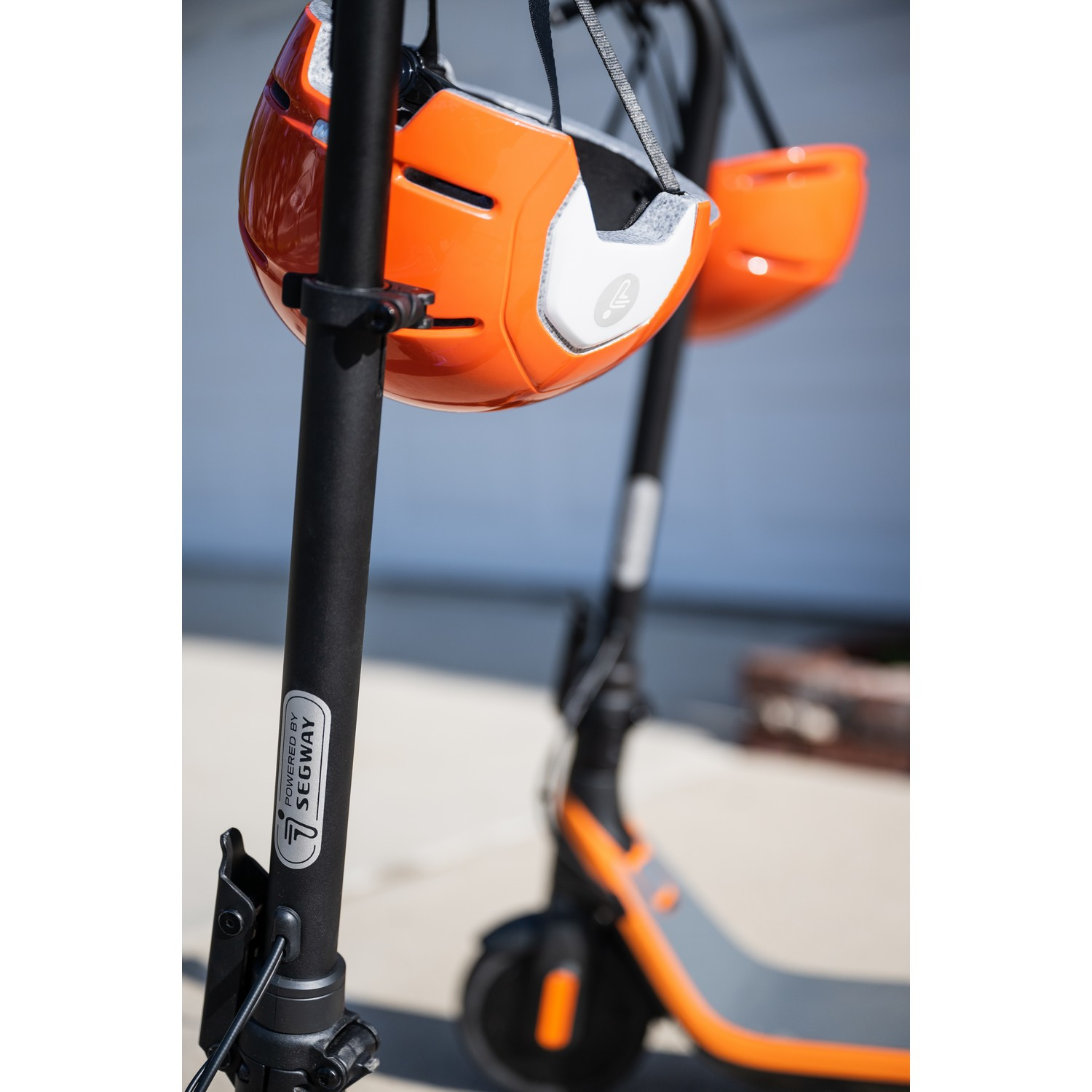 Oranje helm hangt aan een oranje en zwarte scooter. De scooter staat op een betonnen oppervlak.