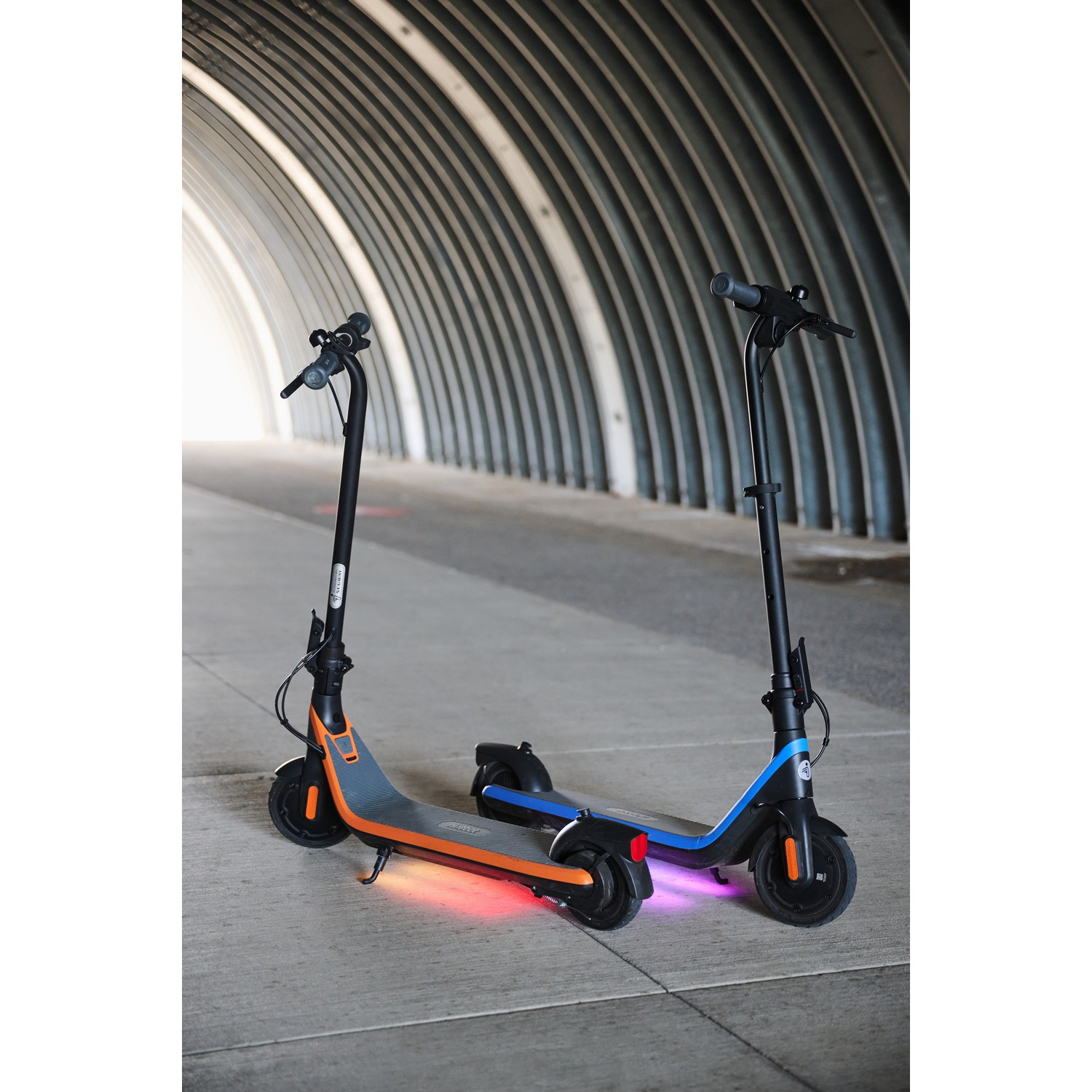 Twee elektrische scooters onder een gewelfde tunnel. Eén is oranje en de andere is blauw.