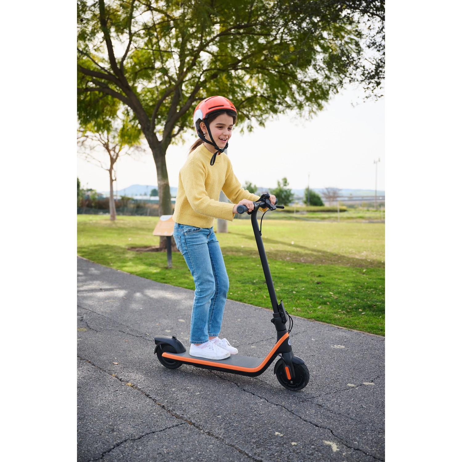Meisje op een elektrische step op een pad, met een helm.