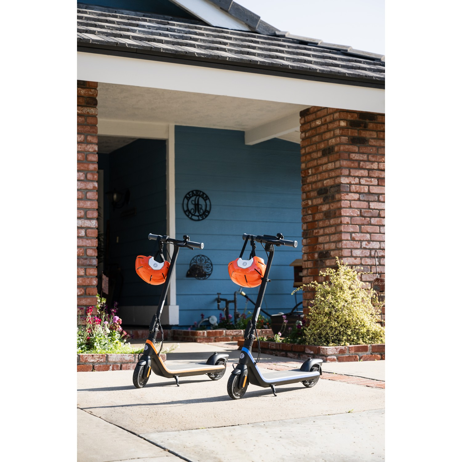 Twee scooters geparkeerd voor een huis, met helmen eraan.