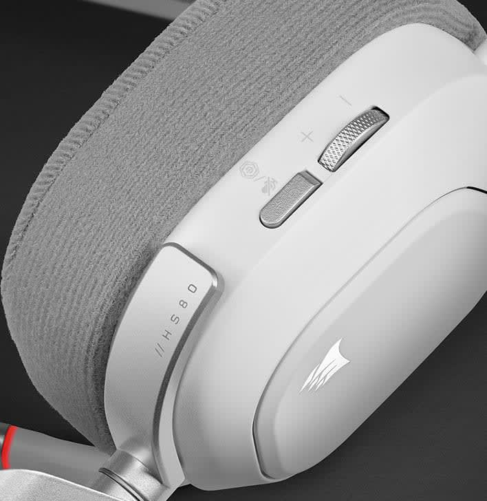 Egy fehér gamer fejhallgató közeli képe hangerőszabályzóval és márkajelzéssel, sötét háttéren.