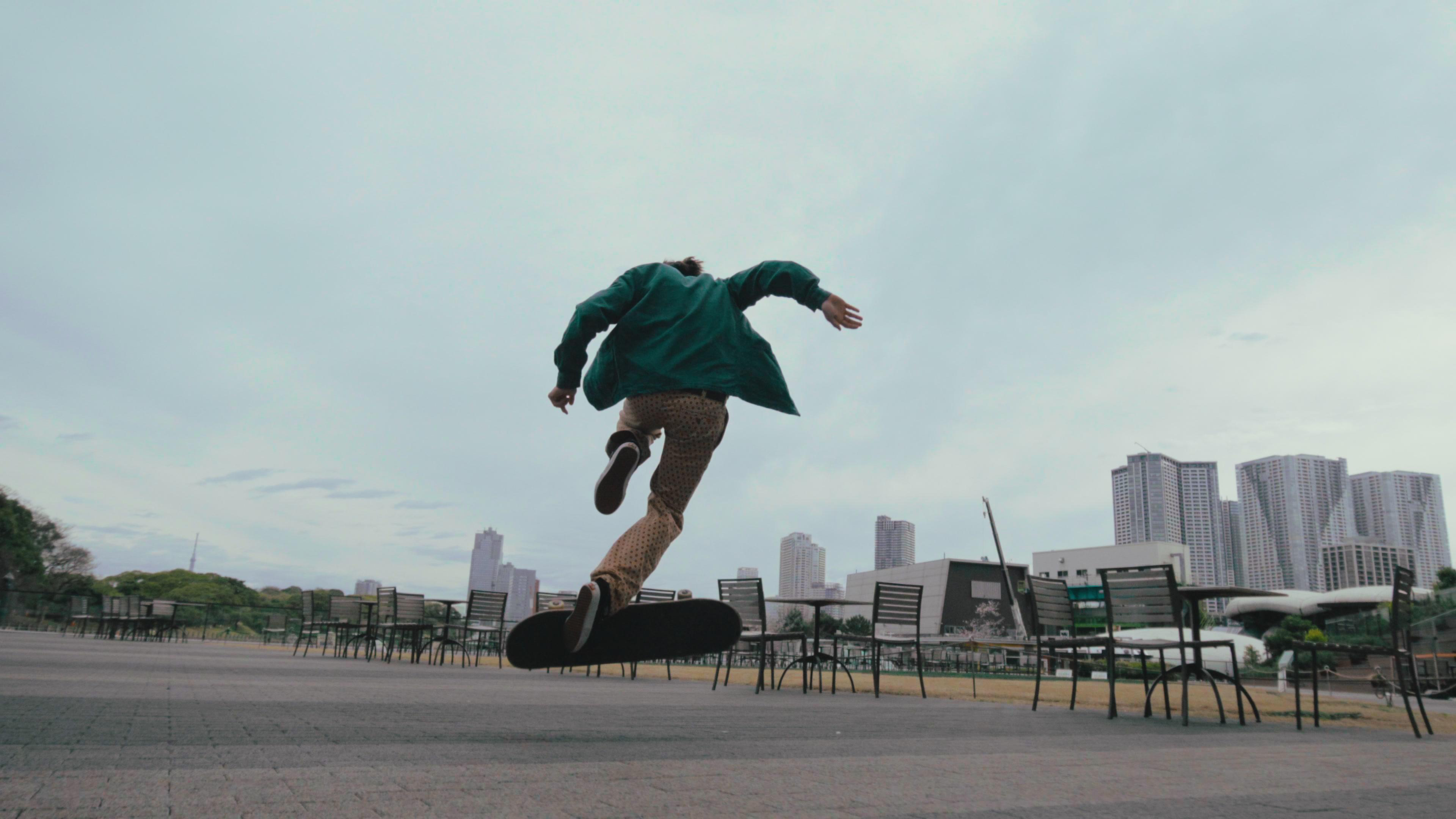 Skateboarder in der Luft vor Wolkenhimmel, Gebäude im Hintergrund.