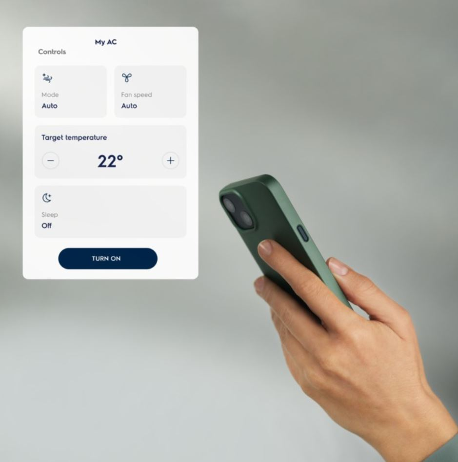 El, klima kontrol ekranını gösteren telefonu tutuyor. Gri arka plan.