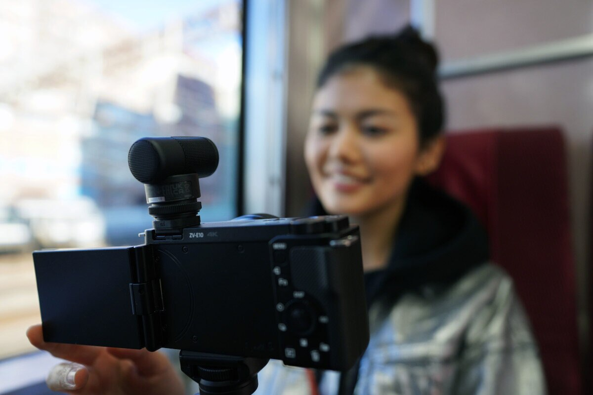 Kobieta nagrywa wideo kamerą w pociągu. Do kamery jest podłączony mikrofon.