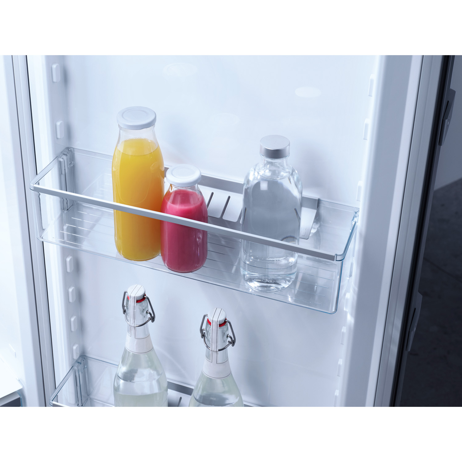 Interno del frigorifero con bottiglie di succo e acqua sugli scaffali.