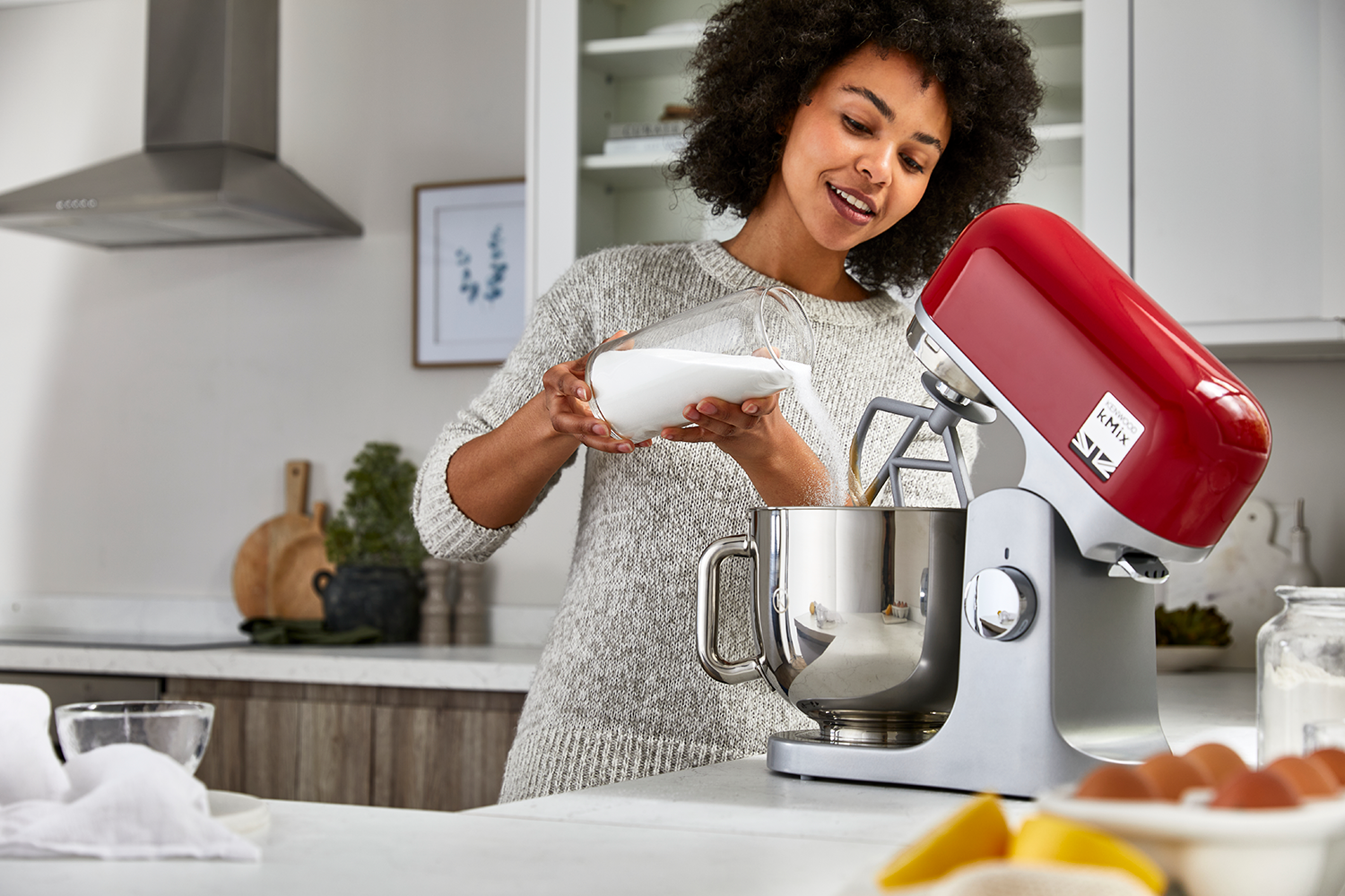Vrouw giet witte vloeistof in een rode mengkom in de keuken. Keuken op de achtergrond.