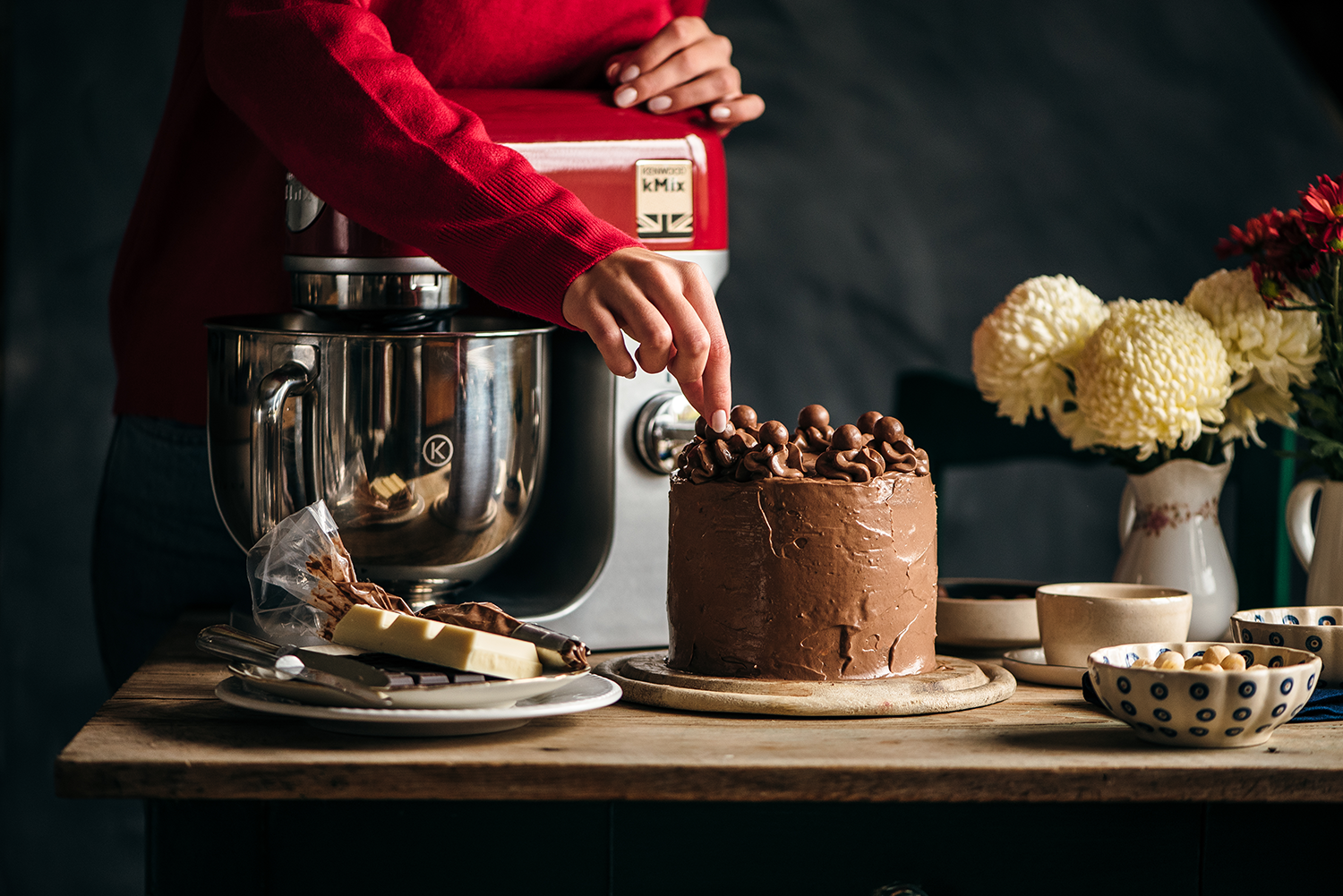 Persoon versiert chocoladetaart met rode mixer op de achtergrond.