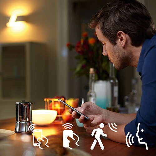 Mężczyzna korzystający z telefonu z ikonami sterowania inteligentnym domem i oświetleniem.