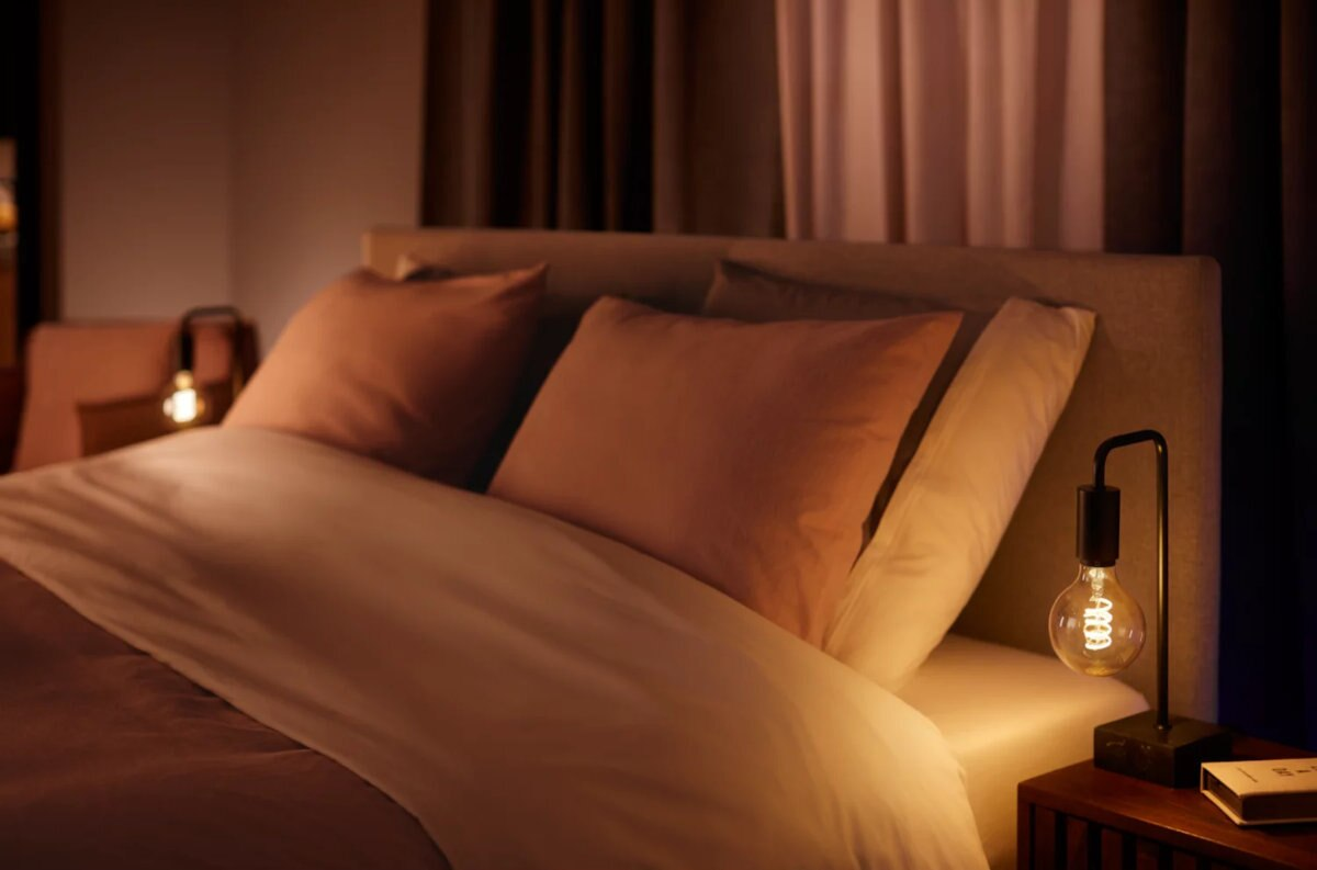 Scena sypialni z łóżkiem, poduszkami, lampą z żarówką i ciemnym tłem.