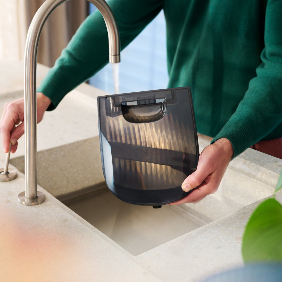 Osoba myjąca czarny filtr odkurzacza pod kranem w zlewie.