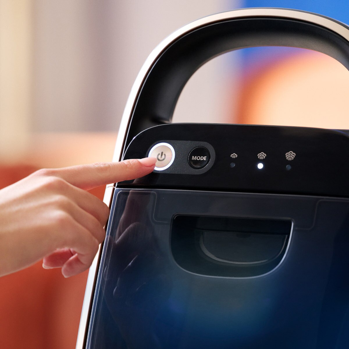 Palec osoby naciska przycisk na czarnym urządzeniu, z 'trybem' i lampkami kontrolnymi.
