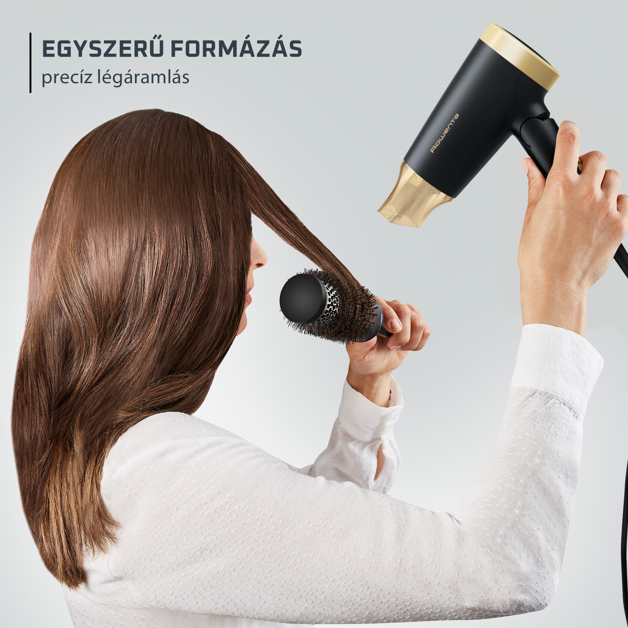 Egy nő hajszárítóval és kefével formázza hosszú, barna haját.
