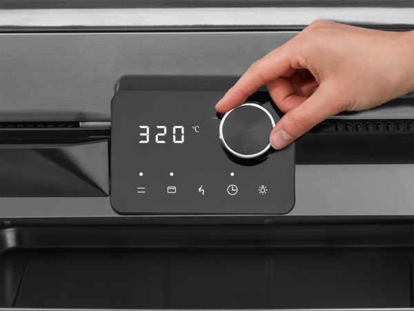 Egy kéz elfordít egy sütőgombot. A kijelző 320°C-ot mutat. A panelen különböző ikonok láthatók.