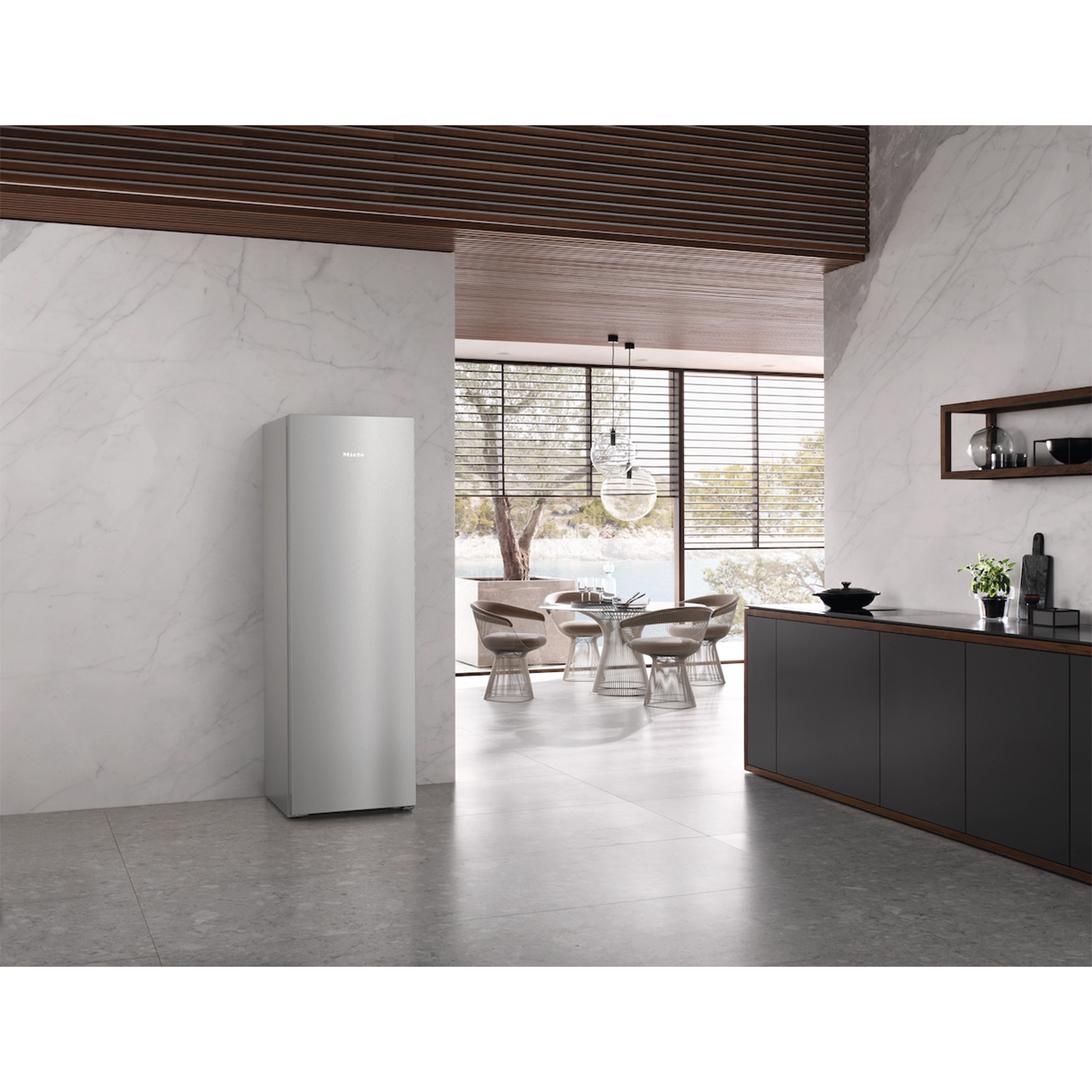Cucina moderna con frigorifero argentato, pareti in marmo, mobili scuri e zona pranzo con vista.