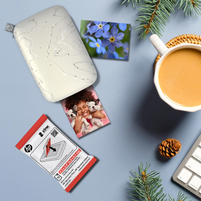 Ein tragbarer Fotodrucker, Fotos und eine Tasse Kaffee auf einer blauen Oberfläche.