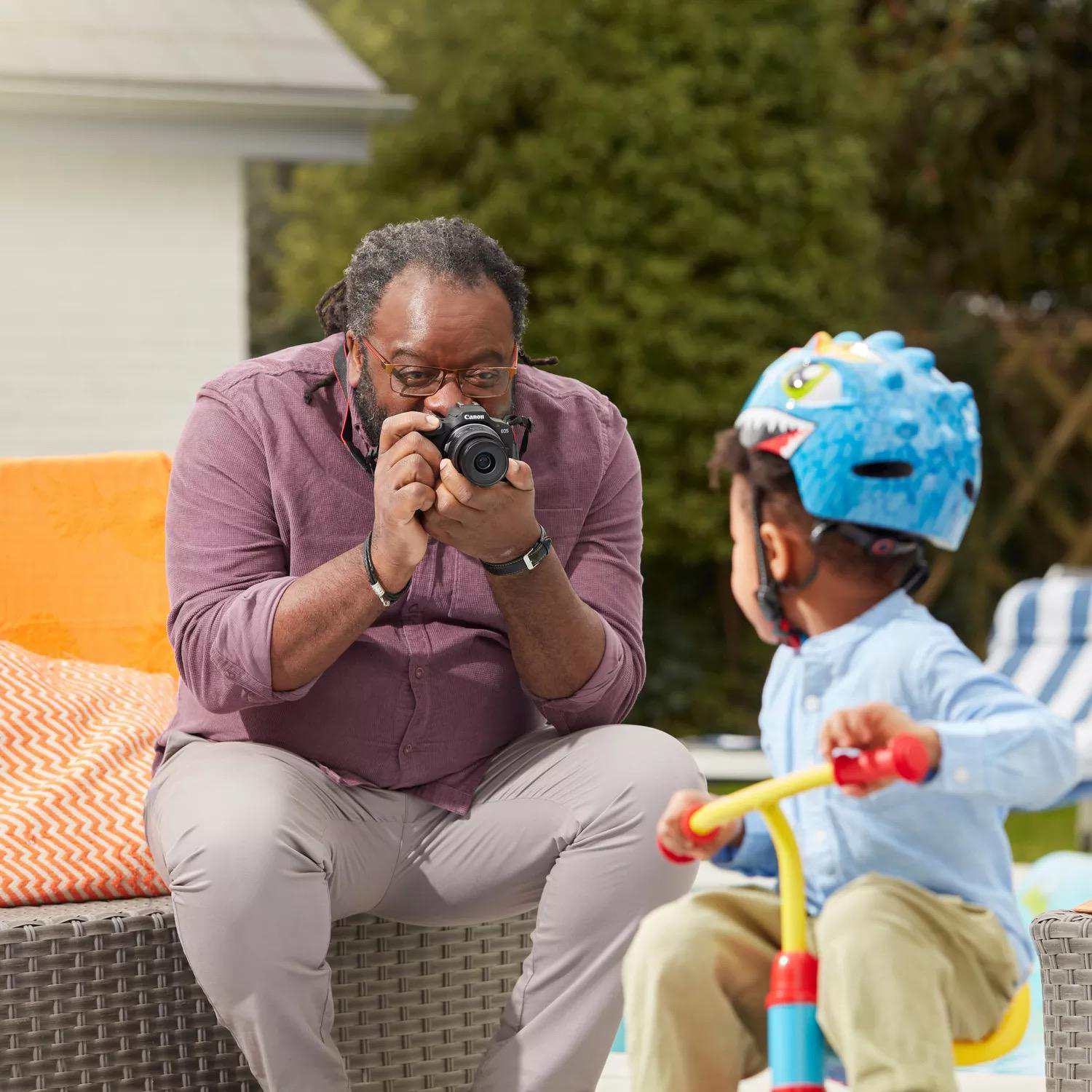 Ein Mann fotografiert ein Kind mit Helm im Freien mit einer Kamera.