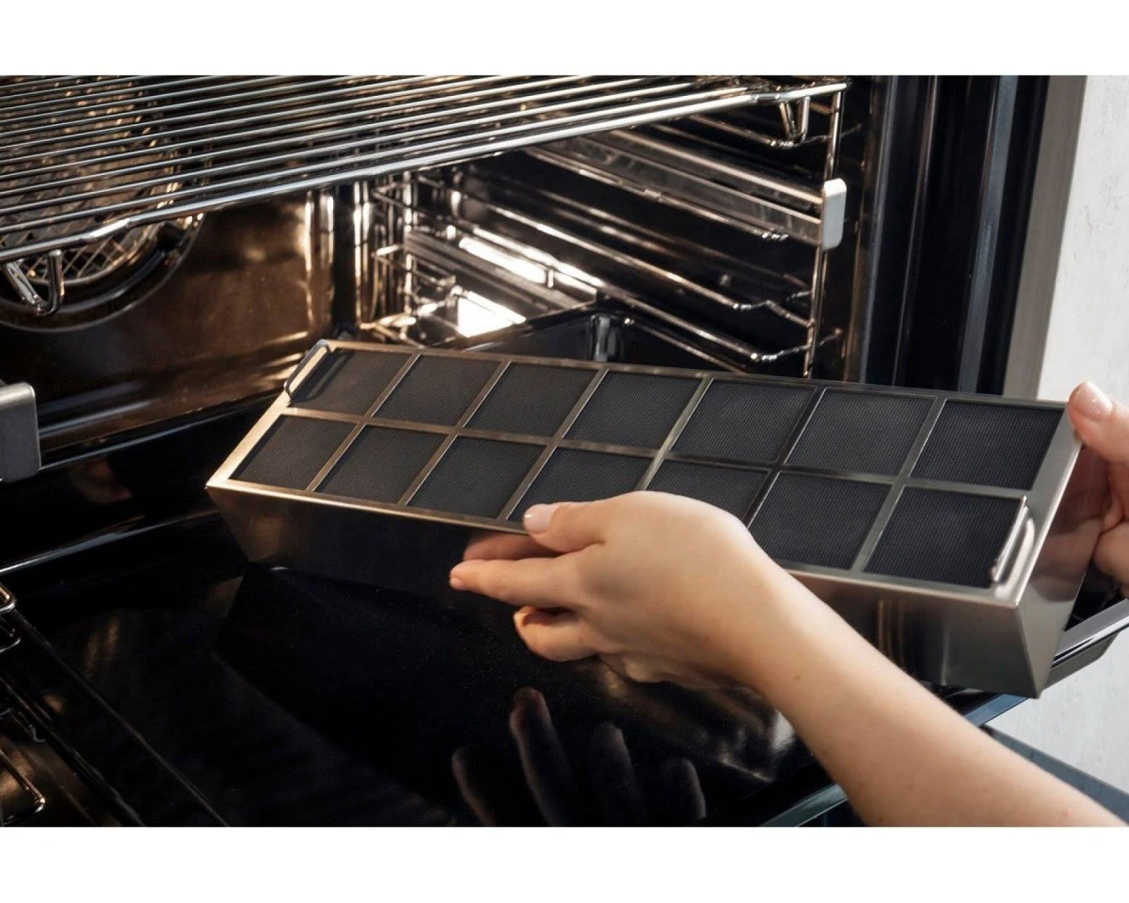 Manos quitando un filtro de un horno. Interior negro del horno.