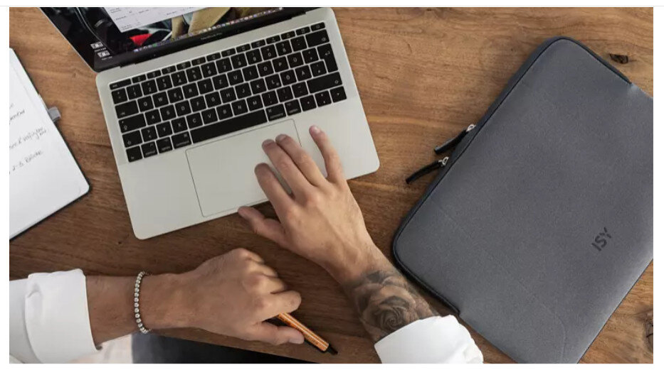 Ręce osoby na laptopie i szara torba na laptopa na drewnianym stole.