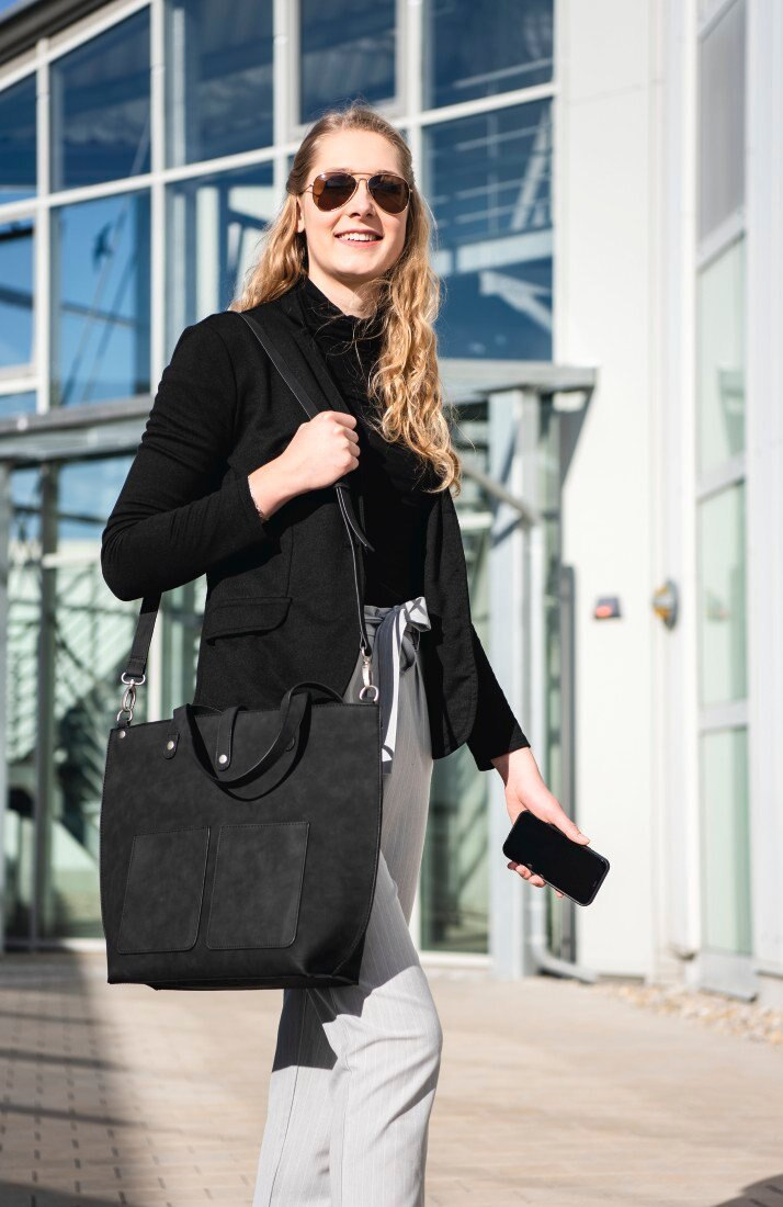 Kobieta w okularach, czarna torba, spaceruje przed budynkiem.