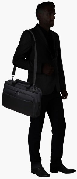 Mężczyzna w garniturze niesie czarną teczkę na ramieniu, widoczny w sylwetce.