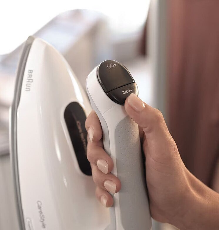 Dłoń trzymająca żelazko. Żelazko jest białe, a uchwyt ma czarny przycisk.