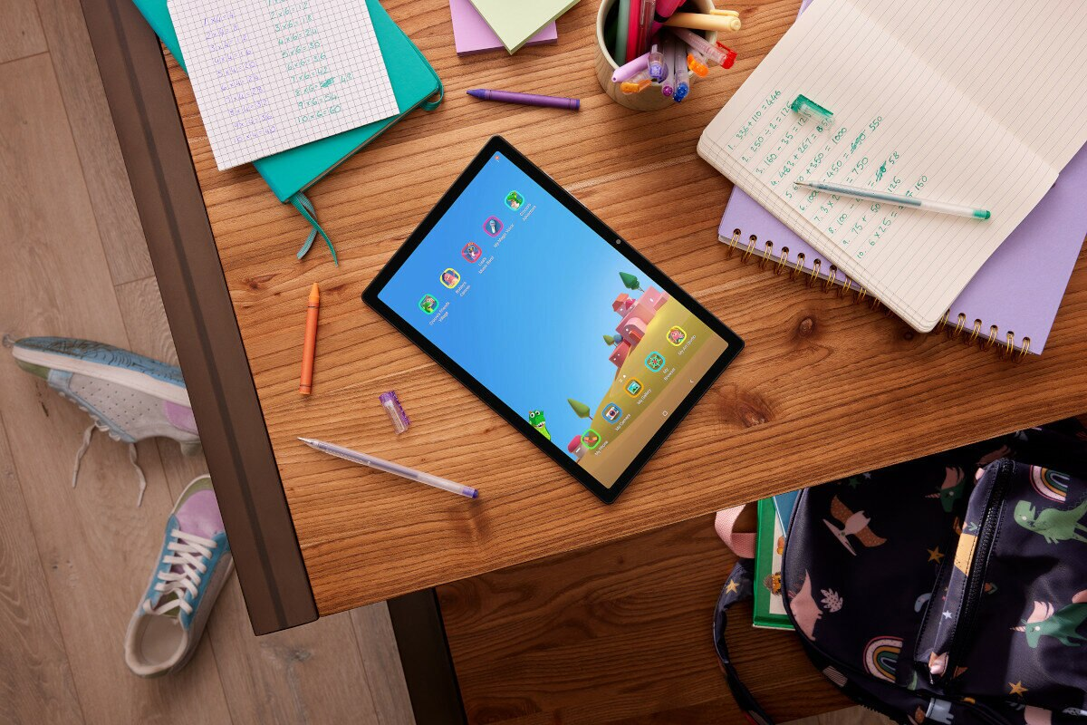 Tablet na drewnianym biurku z artykułami szkolnymi: długopisami, kredkami, notatnikami i plecakiem.