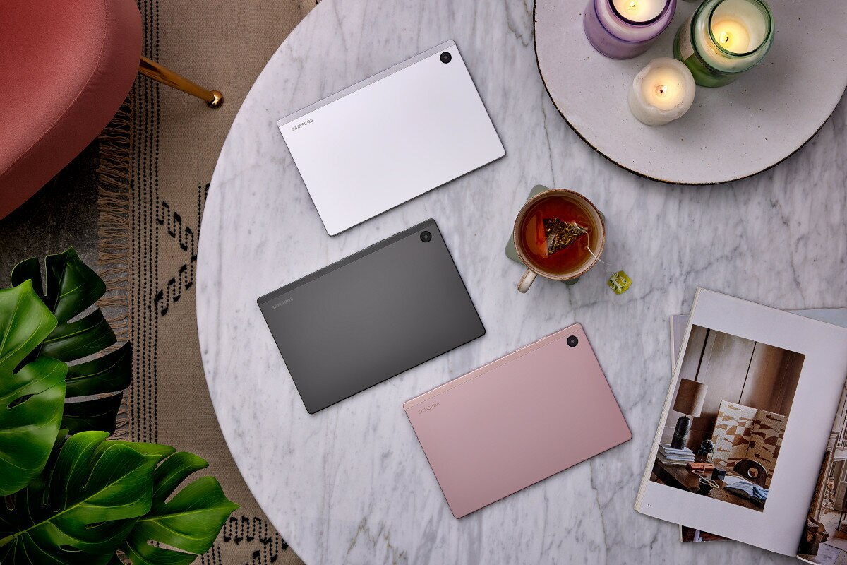 Trzy tablety w kolorze srebrnym, szarym i różowym na marmurowym stole z dekoracjami.