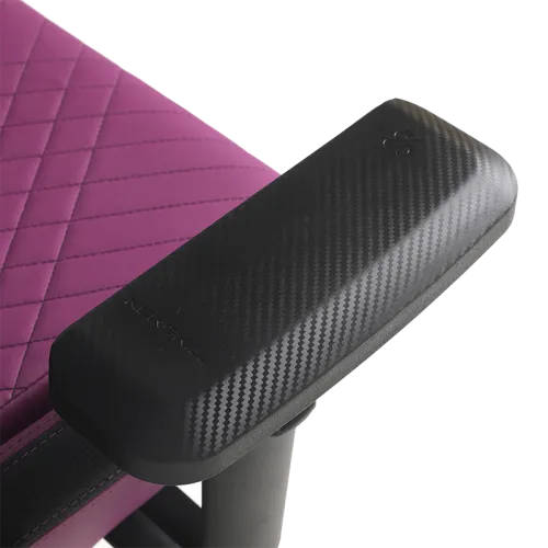 Primer plano de un reposabrazos de fibra de carbono negro en una silla de juego acolchada magenta.