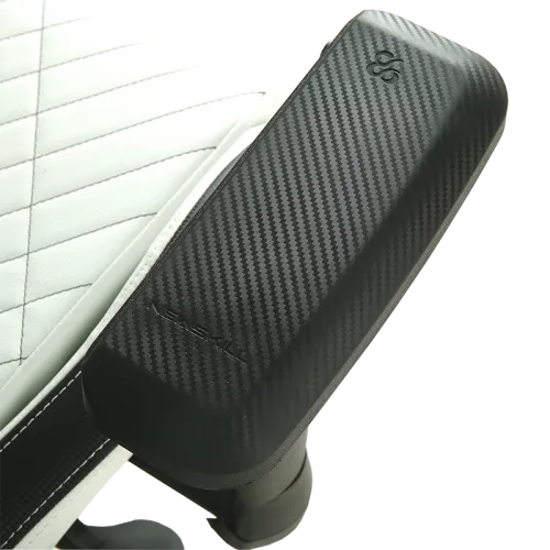 Dispositivo de masaje negro y fibra de carbono posicionado en el brazo de una silla acolchada blanca.