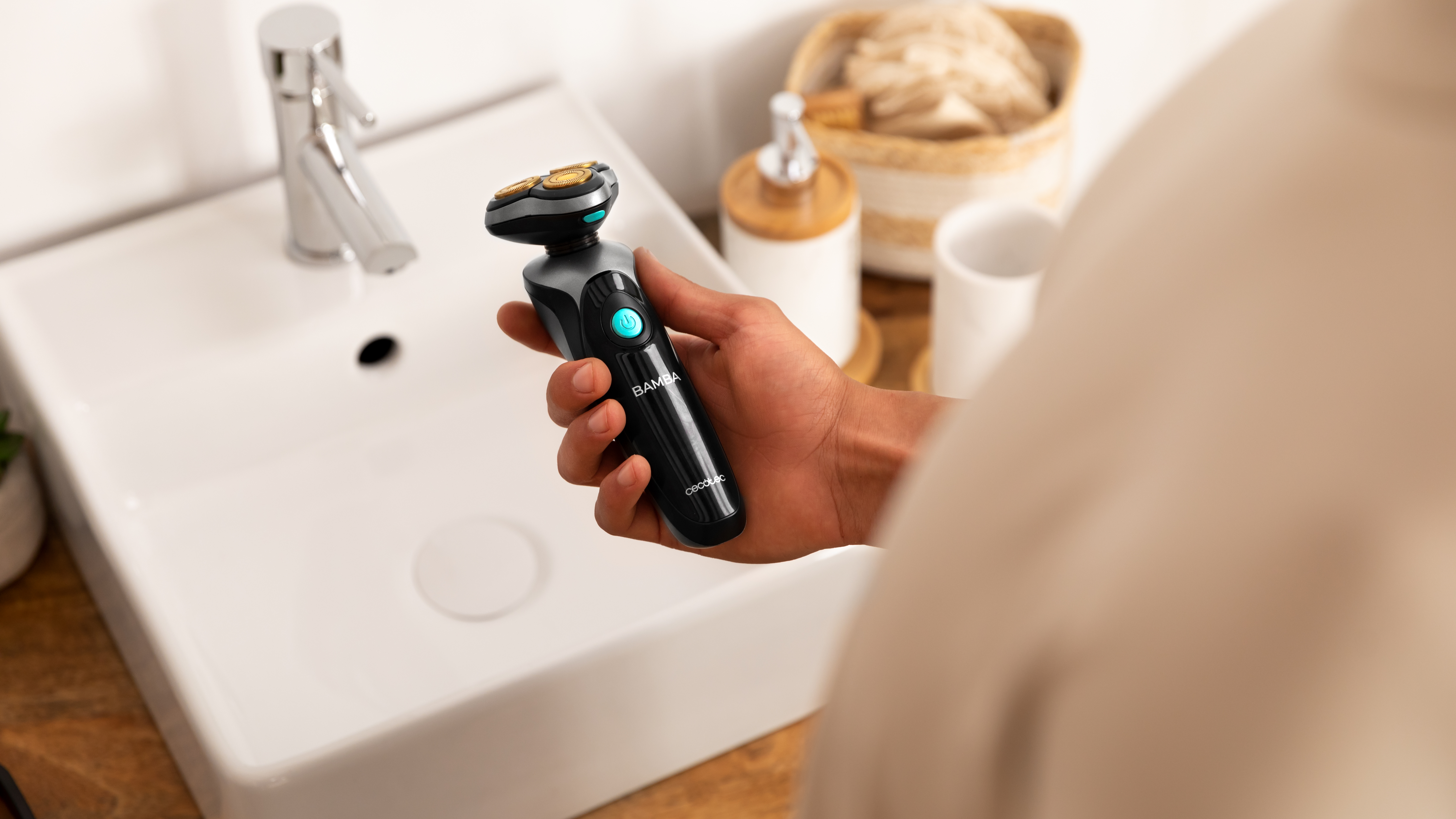 Mano de hombre sosteniendo afeitadora eléctrica negra y gris sobre lavabo blanco. Baño.