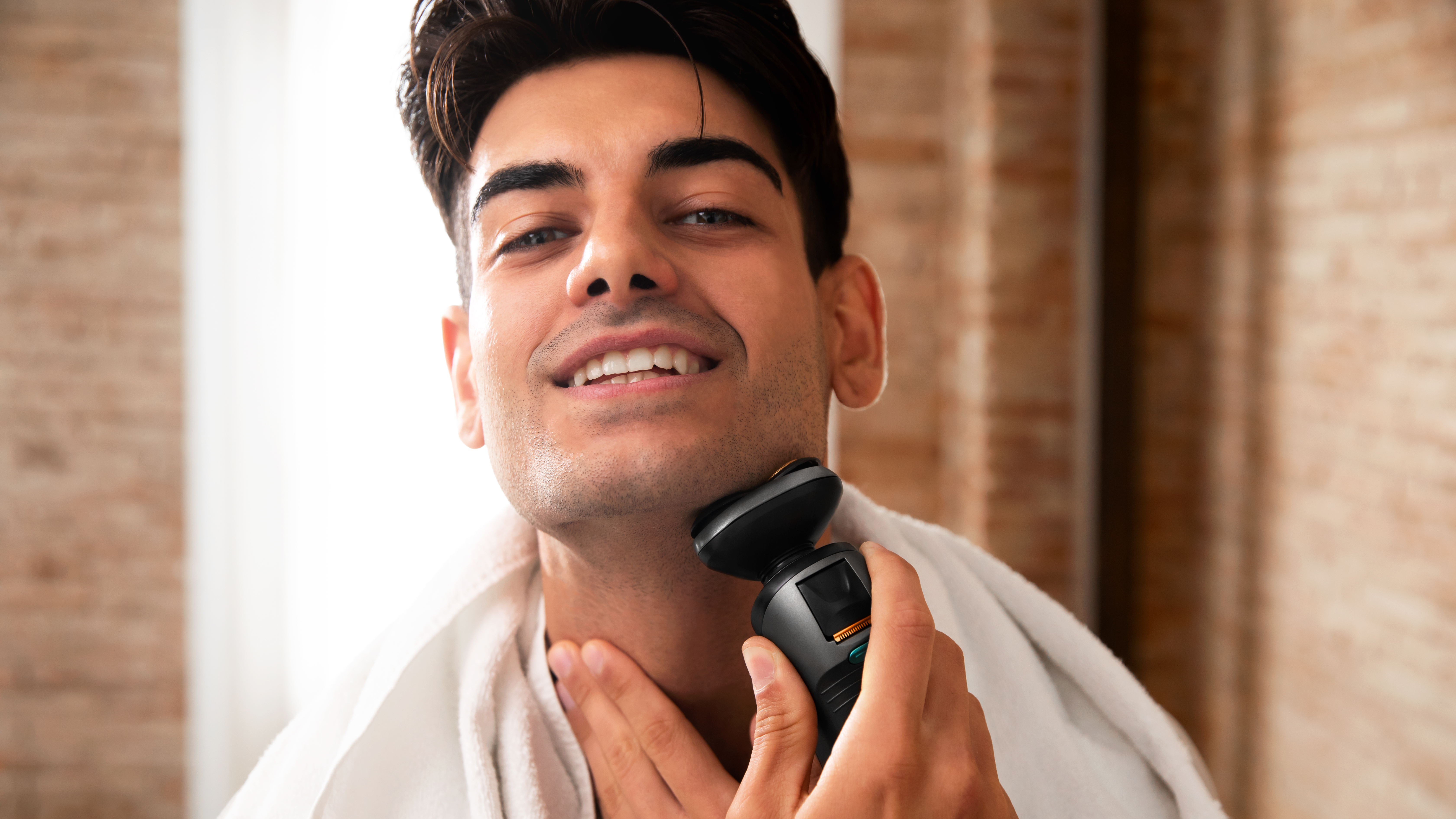 Un hombre se afeita la cara con una afeitadora eléctrica, sonriendo en un baño.
