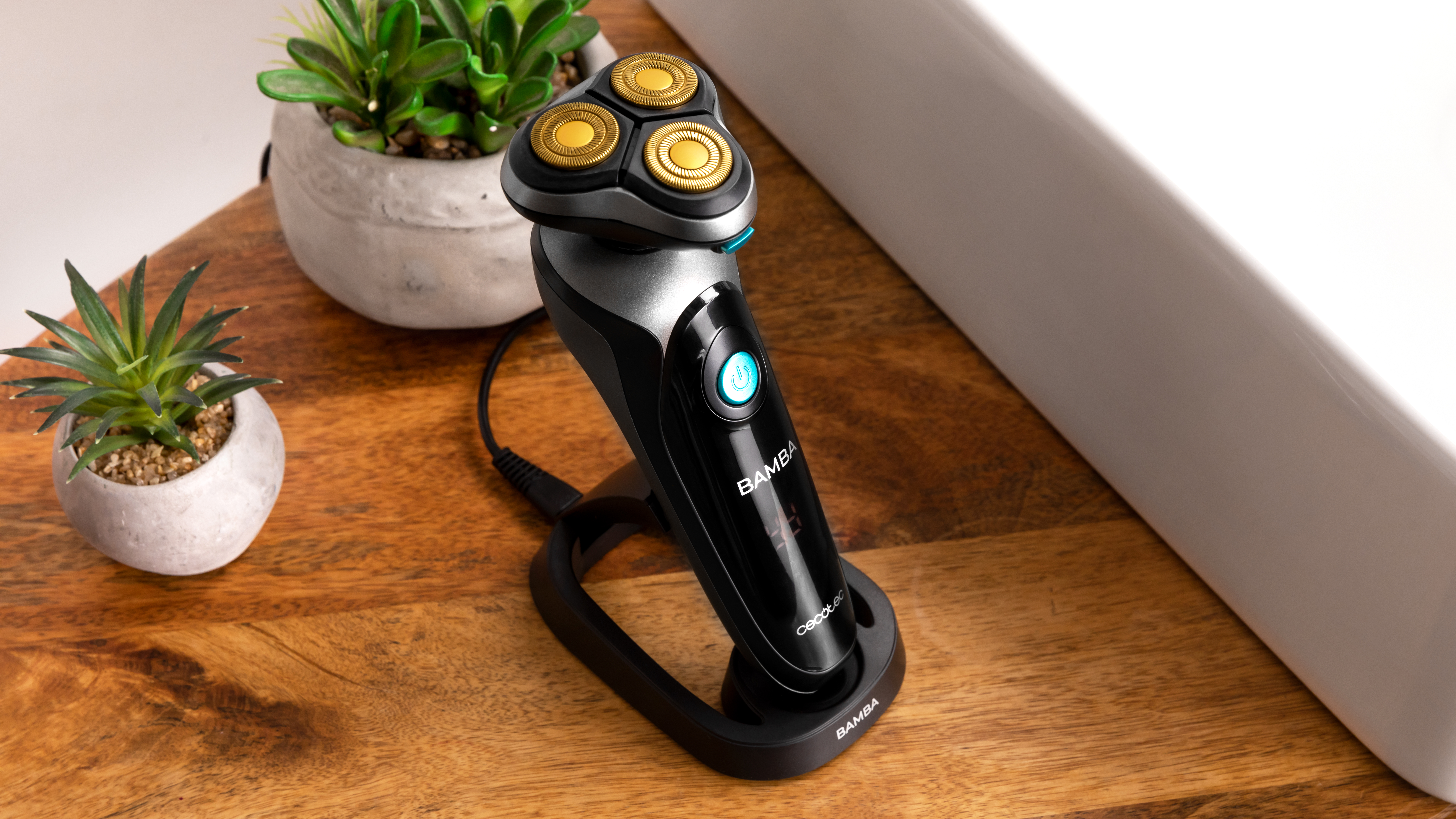 Afeitadora eléctrica negra y plateada sobre una base de carga con pequeñas plantas al fondo.