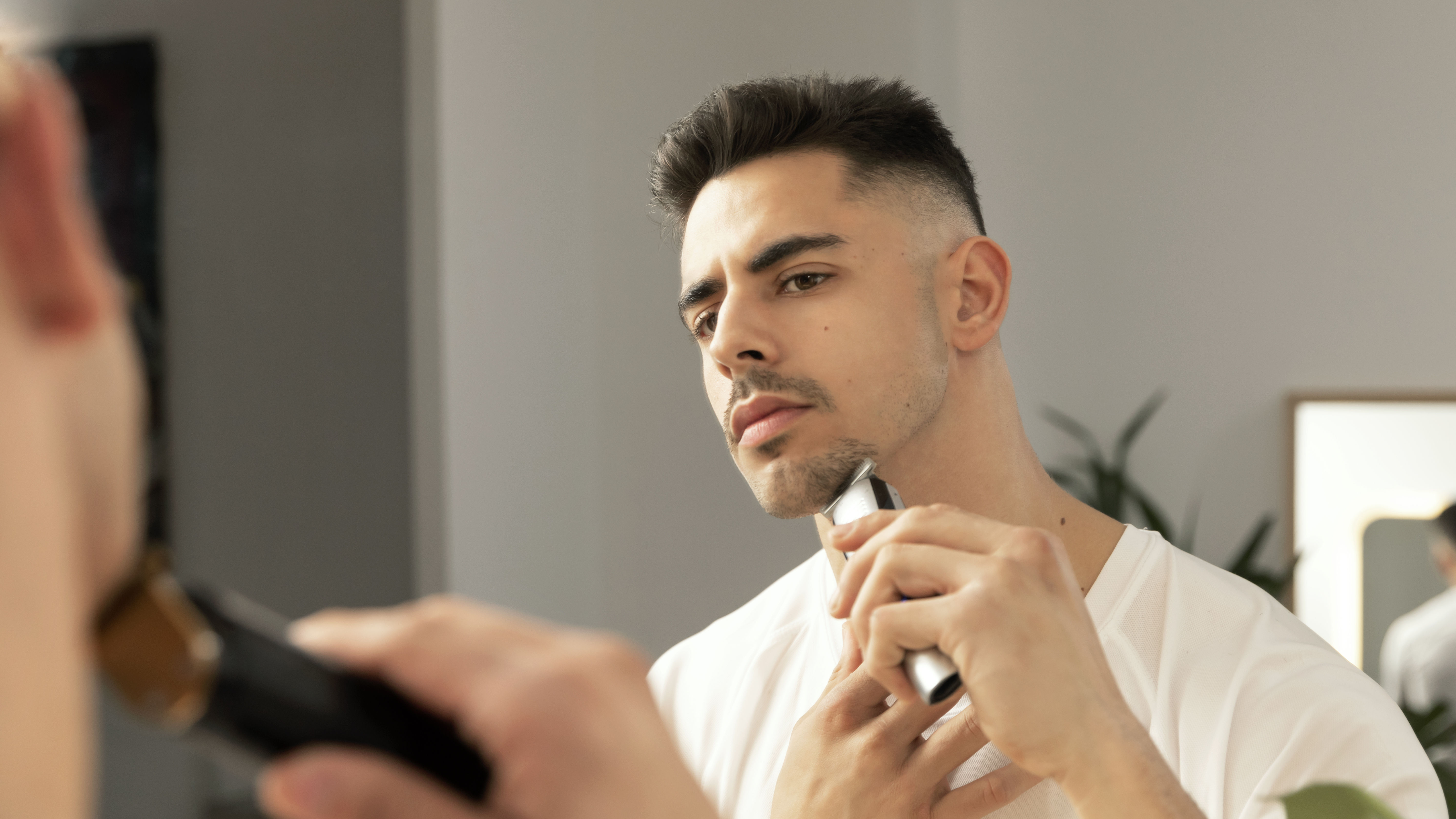 Hombre recortando su barba con un recortador eléctrico, mirándose.