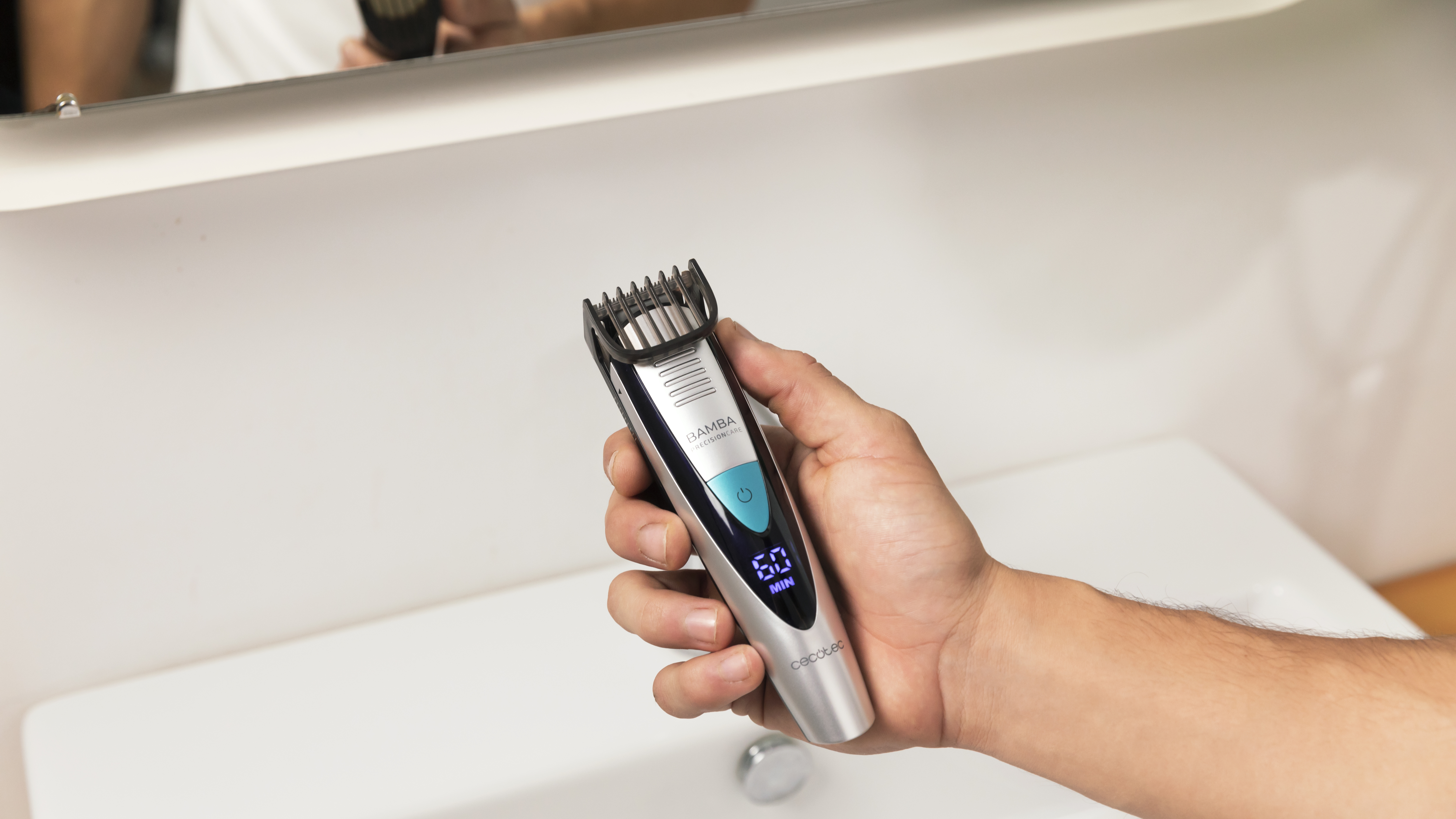 Mano sosteniendo una recortadora de pelo negra y plateada sobre un lavabo blanco, con pantalla digital.