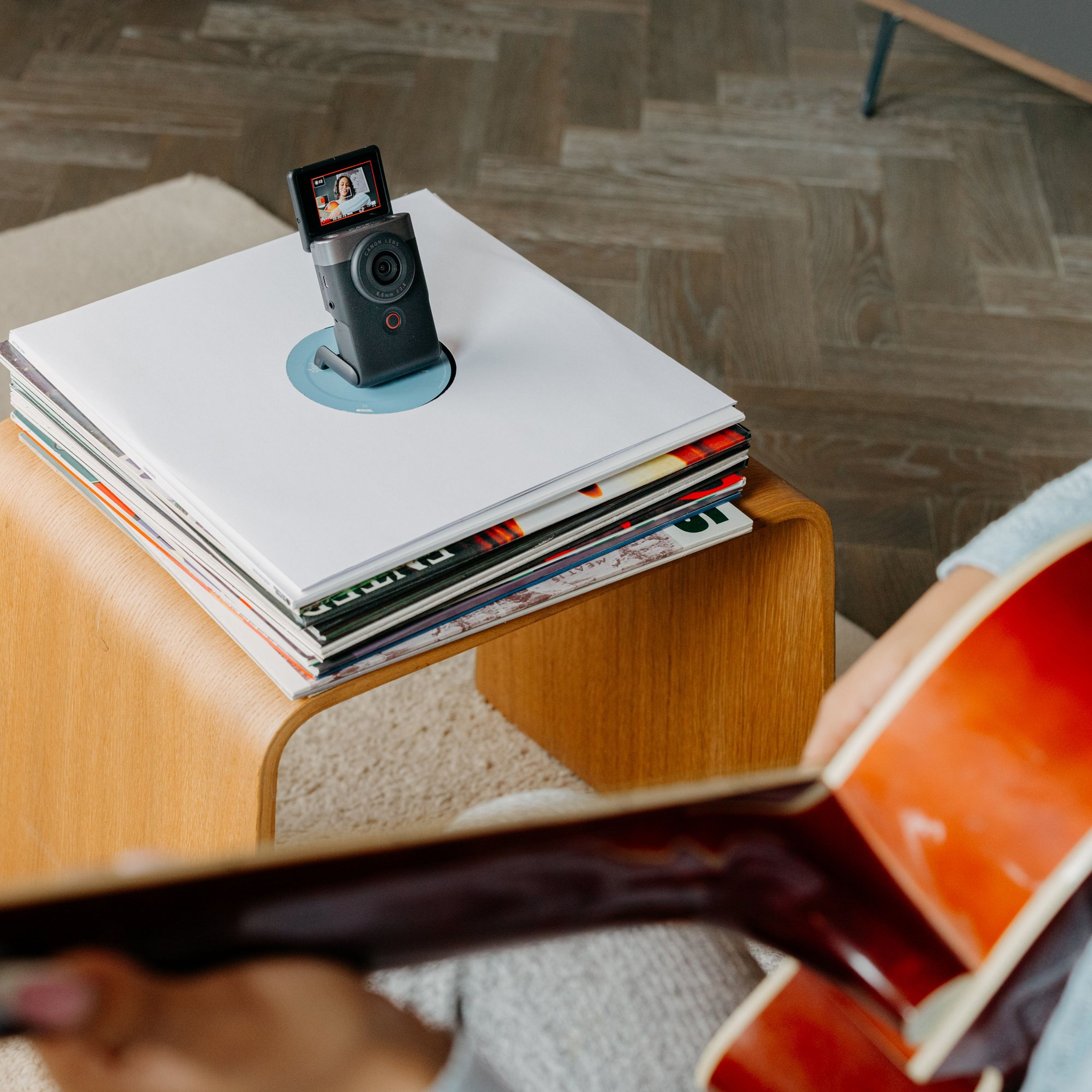 Une caméra est montée sur des disques vinyles. Une personne joue de la guitare en arrière-plan.