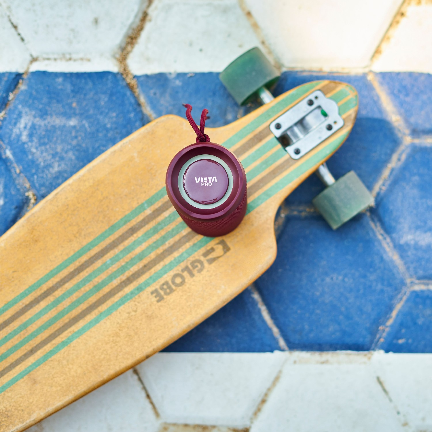 Un altavoz rojo sobre una patineta. El altavoz está sobre una patineta con fondo azul y blanco.