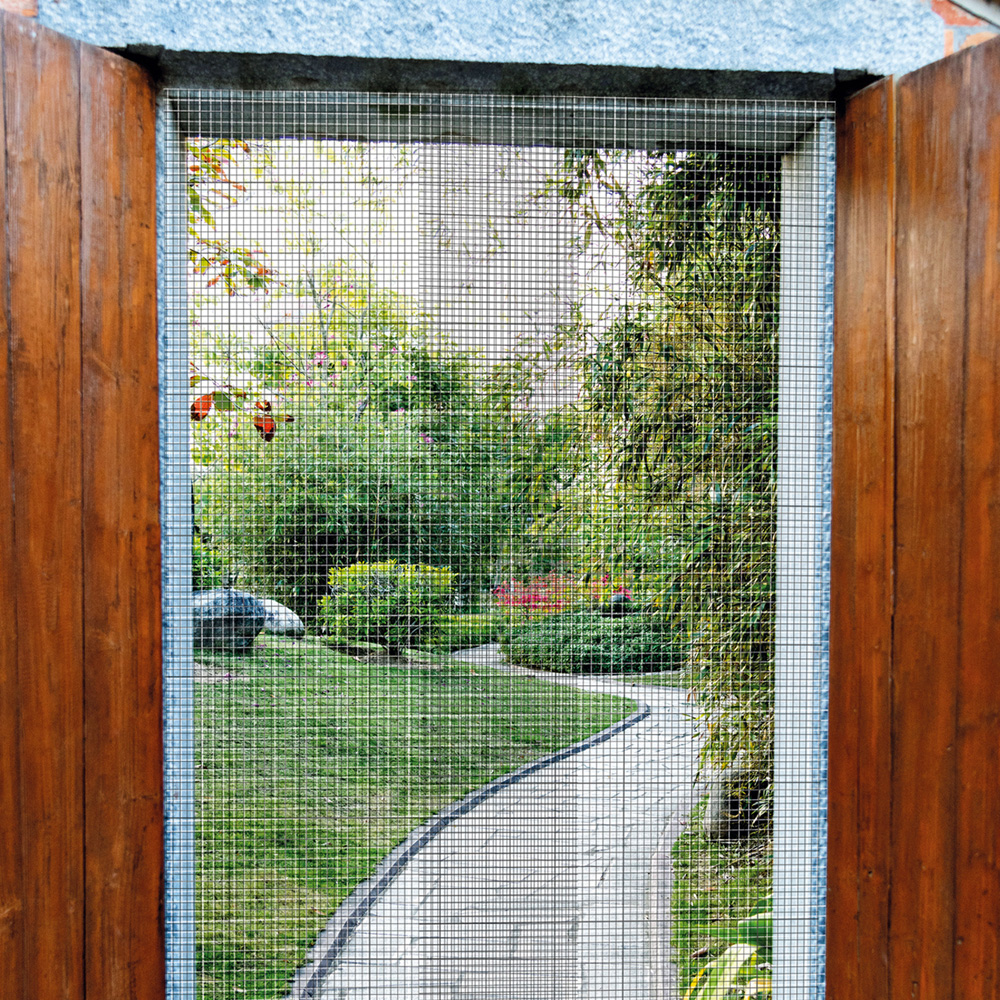 Vista a través de una puerta de madera con pantalla a un jardín soleado con camino de piedra.